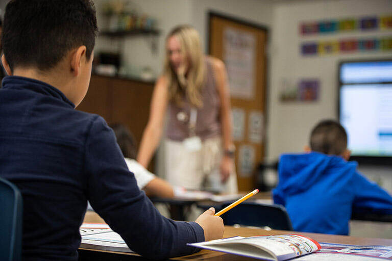 Two students sitting at a desk while a professor is walking around the classroom