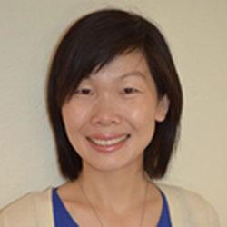 A smiling woman with dark brown hair in a white blouse and blue shirt.