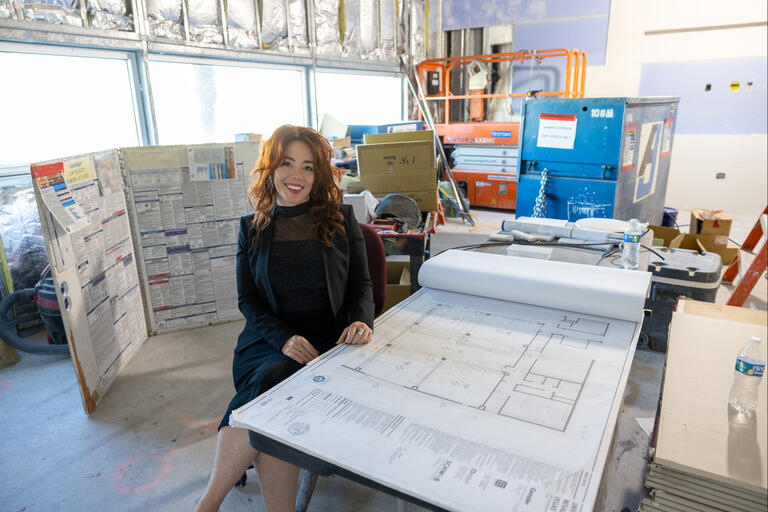 Aundrea Frahm sits at table with blueprint laid over it